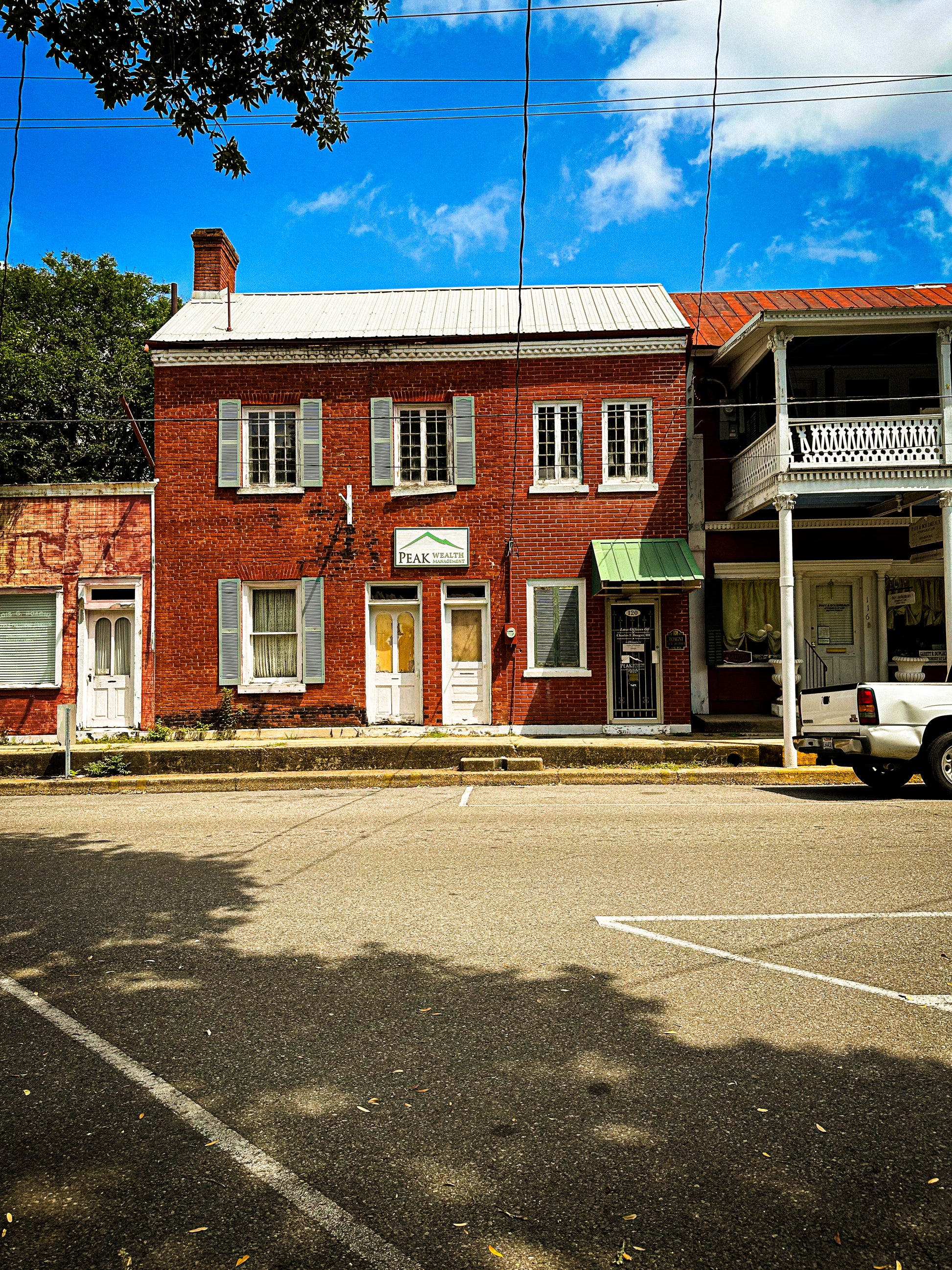 Historic Louisiana Red brick building with white doors and green awnings on a sunny day.