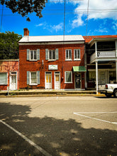 Load image into Gallery viewer, Historic Louisiana Red brick building with white doors and green awnings on a sunny day.